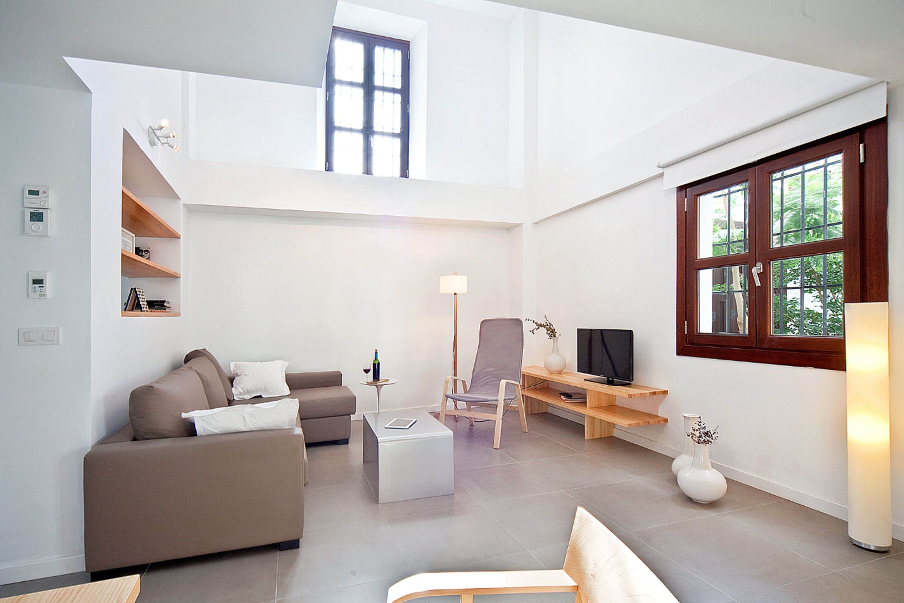 Una sala de estar moderna con techo alto, un sofá, una mesa de centro, un televisor y una ventana con vistas a zonas verdes.
