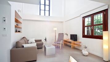 Una sala de estar moderna con techo alto, un sofá, una mesa de centro, un televisor y una ventana con vistas a zonas verdes.