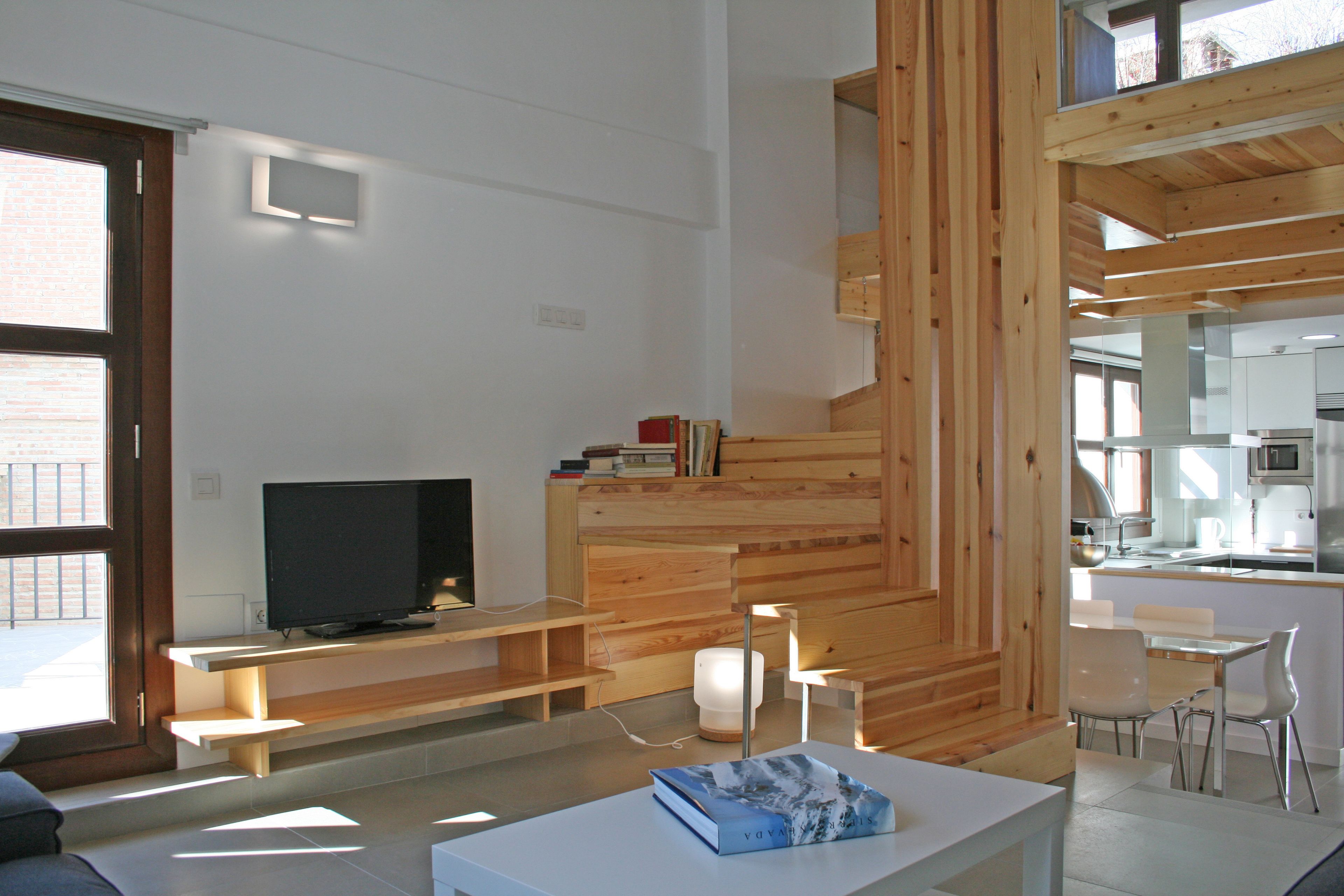 A modern living room with a flat-screen TV, wooden shelves, and a dining area with chairs.