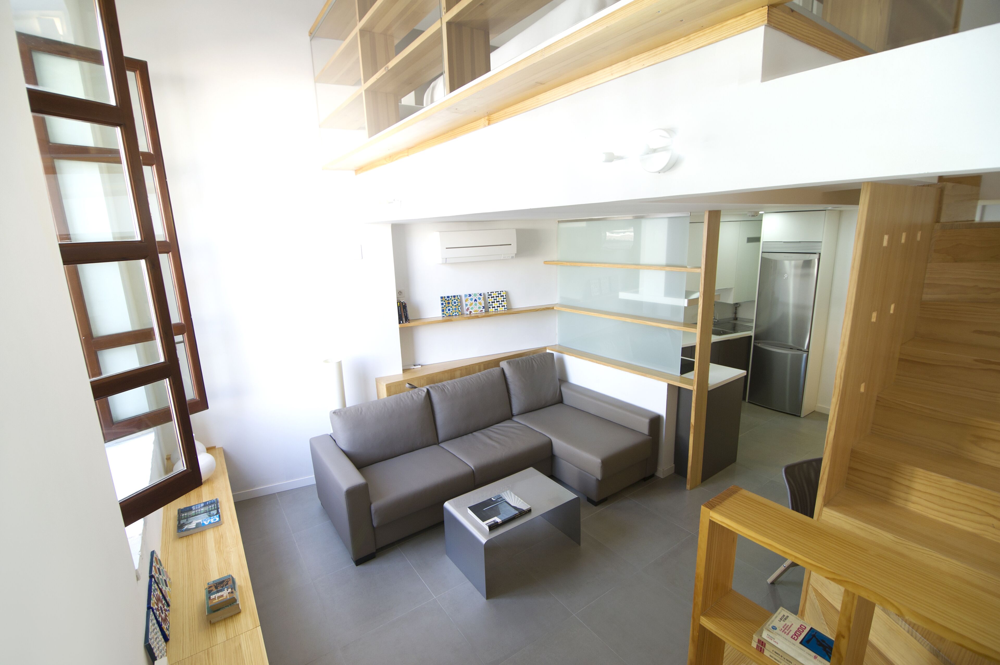 A modern living room with a grey sectional sofa, a small coffee table, and a wooden TV stand. There is a kitchen area visible in the background.