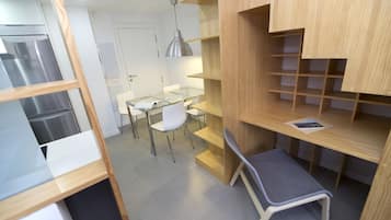 Una cocina compacta con refrigerador incorporado, una mesa de vidrio con sillas y un banco de madera.