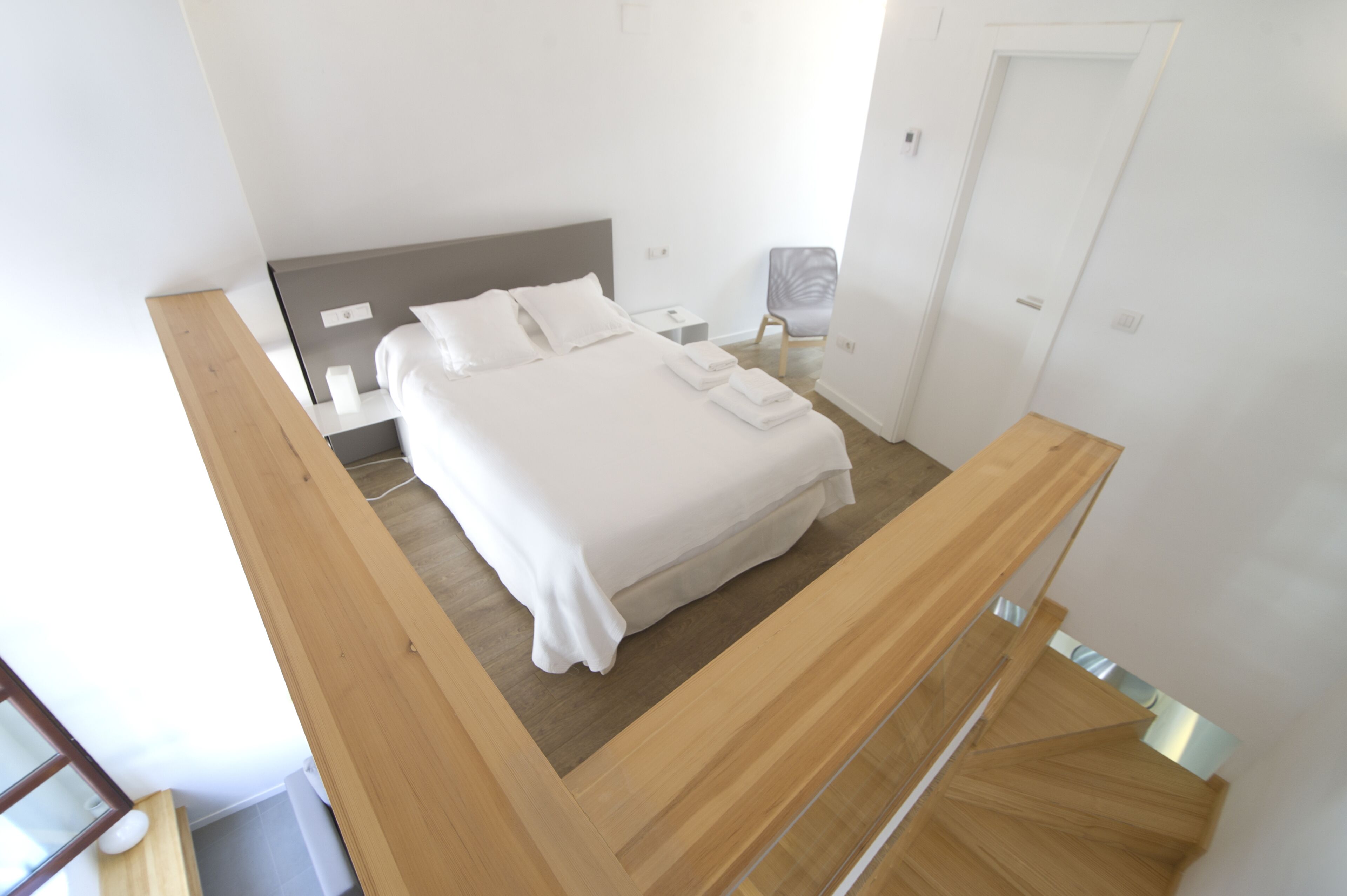 A modern hotel room with a large bed, a wooden headboard, a bedside table, and a chair.