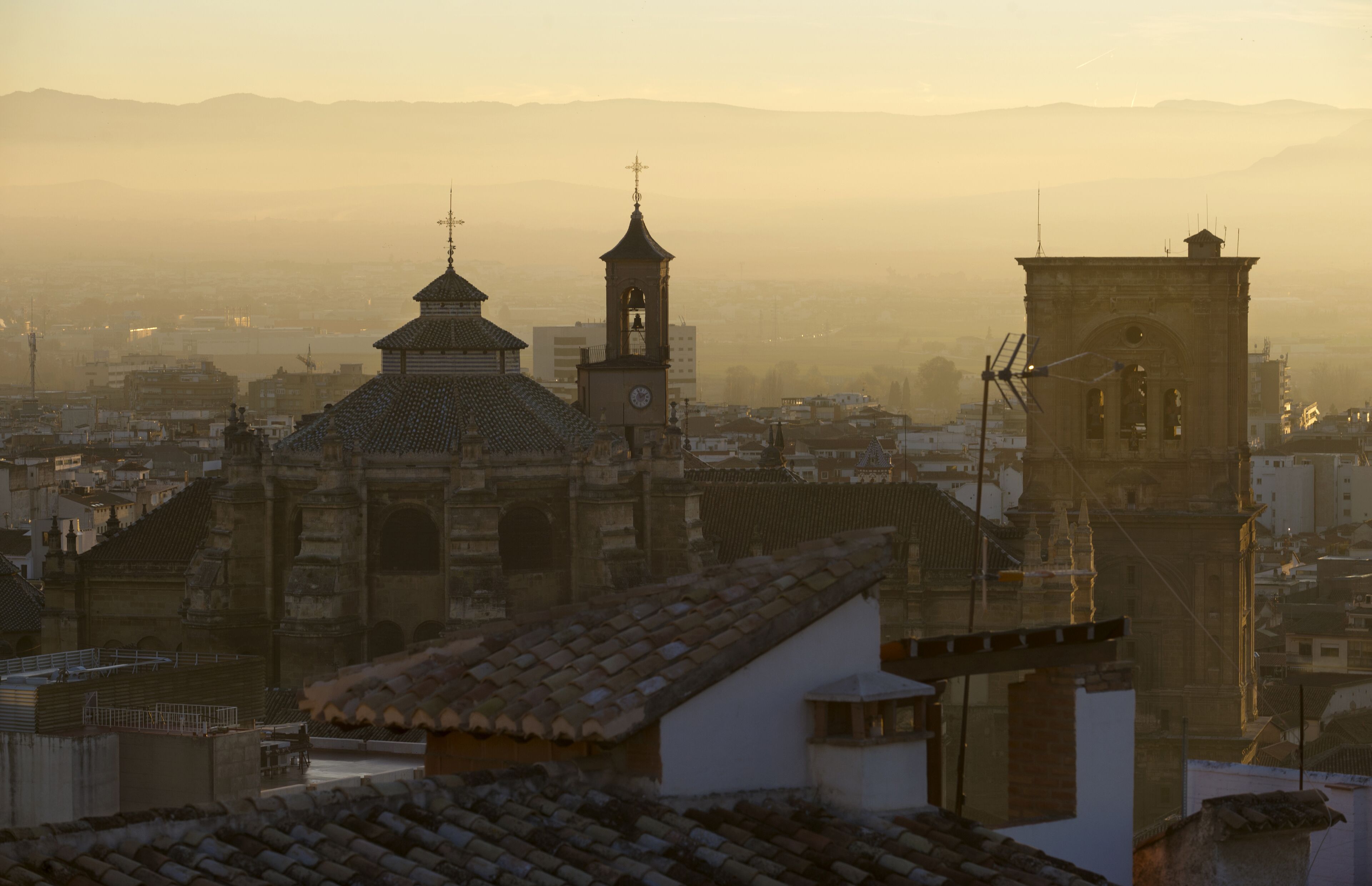 A historic building with a clock tower and domed roof, surrounded by other buildings and mountains in the background.