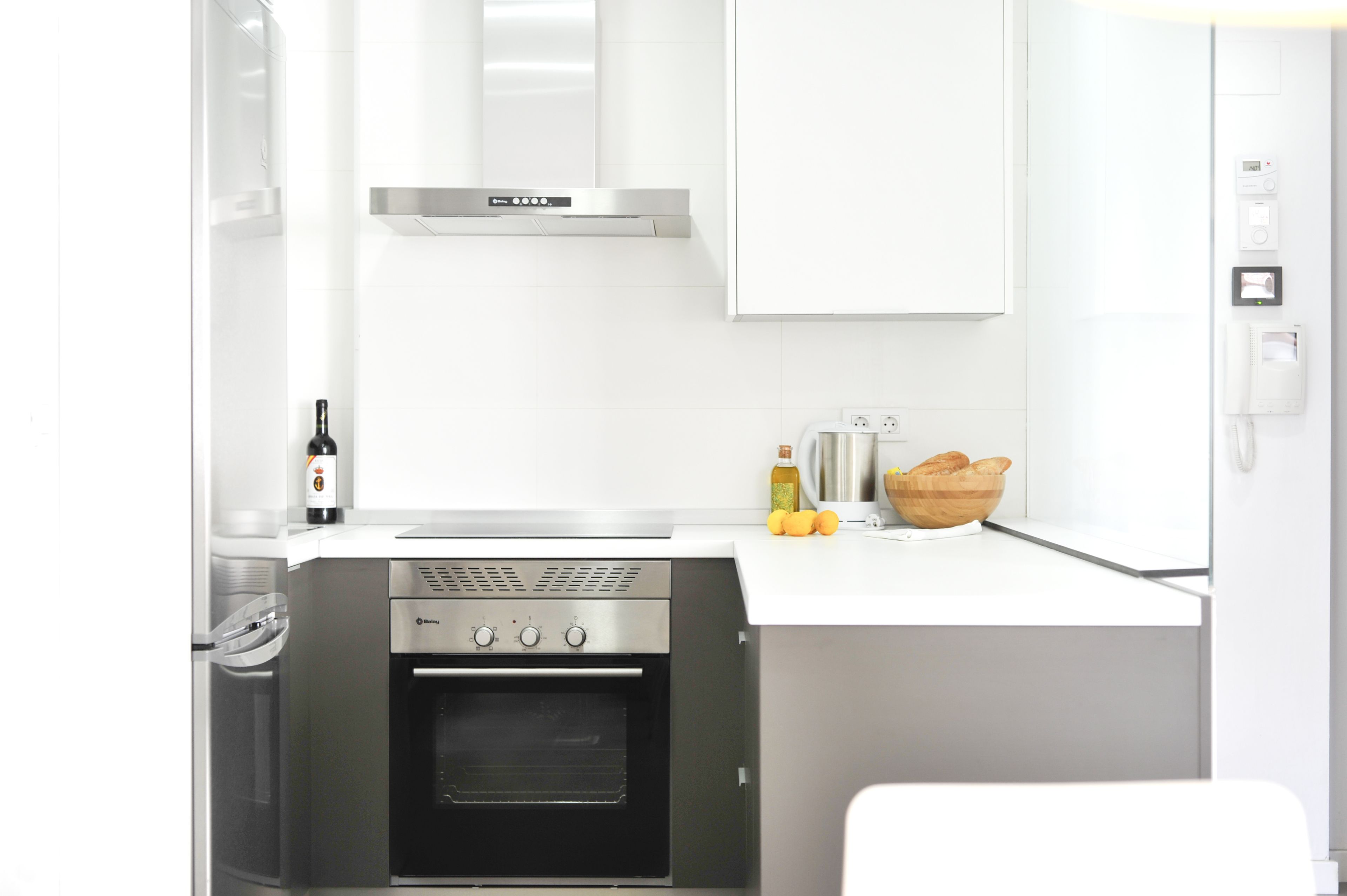 Cocina compacta con horno integrado, extractor de acero inoxidable y encimera blanca.
