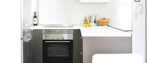 A compact kitchen with a built-in oven, a stainless steel range hood, and a white countertop.