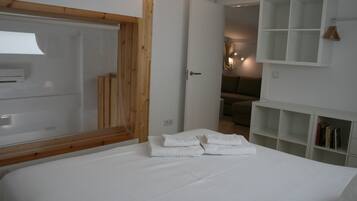 Un dormitorio con una cama grande, cabecera de madera, armario blanco y estante empotrado con libros.