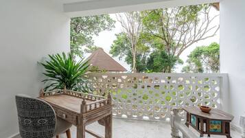 A balcony with a wooden table and chairs, a decorative fence, and a view of trees and a building.