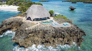 Casa con techo de paja y piscina en una isla rocosa rodeada de aguas azul turquesa.