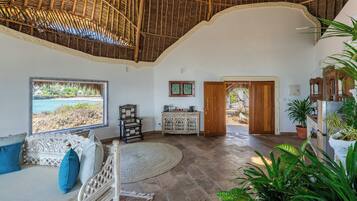 Amplia habitación con un gran ventanal con vistas a la playa, una puerta de madera y un área de estar con alfombra tejida.