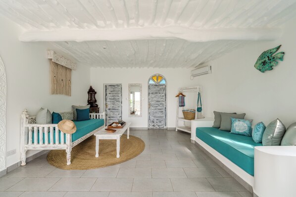 A spacious living area with a white ceiling, a sofa with teal cushions, a white bench, and a woven rug. - Chale Island Resort (Chale Island)