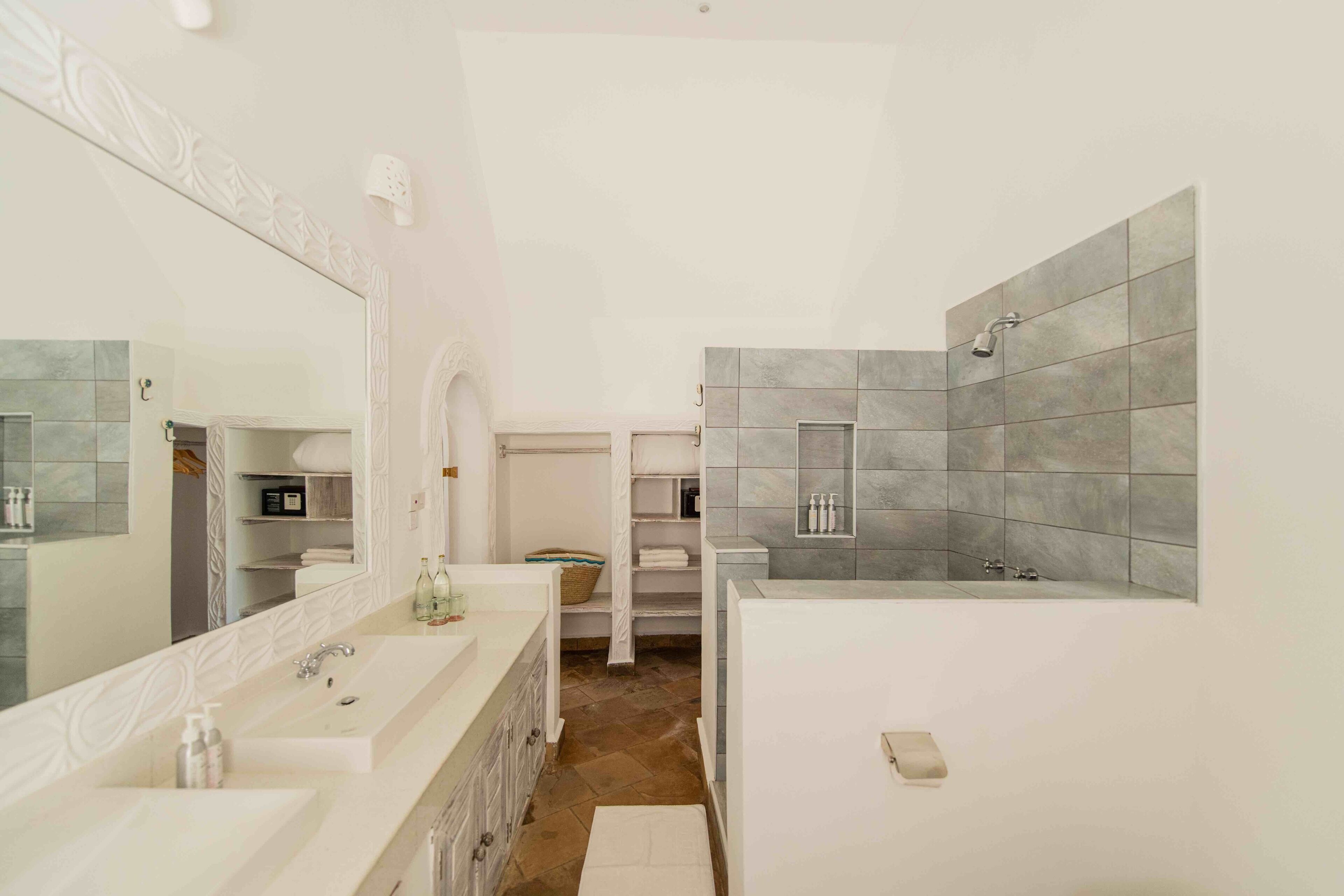 A modern bathroom with a double sink vanity, a large mirror, a built-in shower, and a storage cabinet.