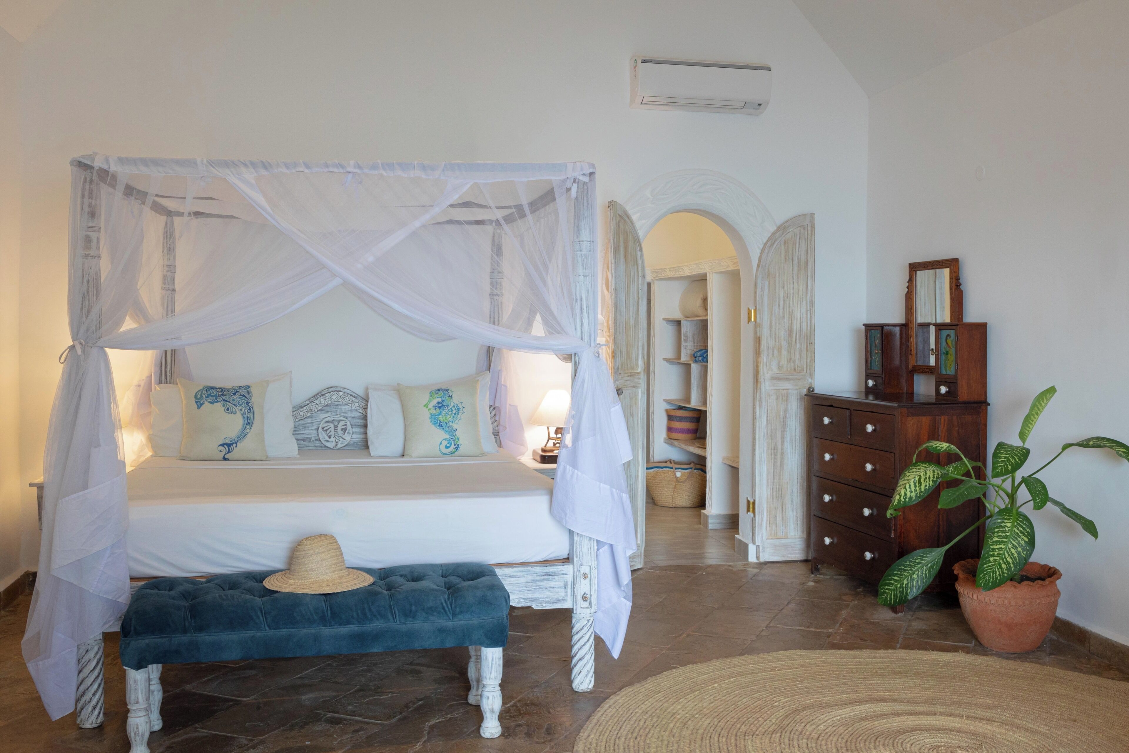 A bedroom with a four-poster bed, a bench, a potted plant, and a dresser.