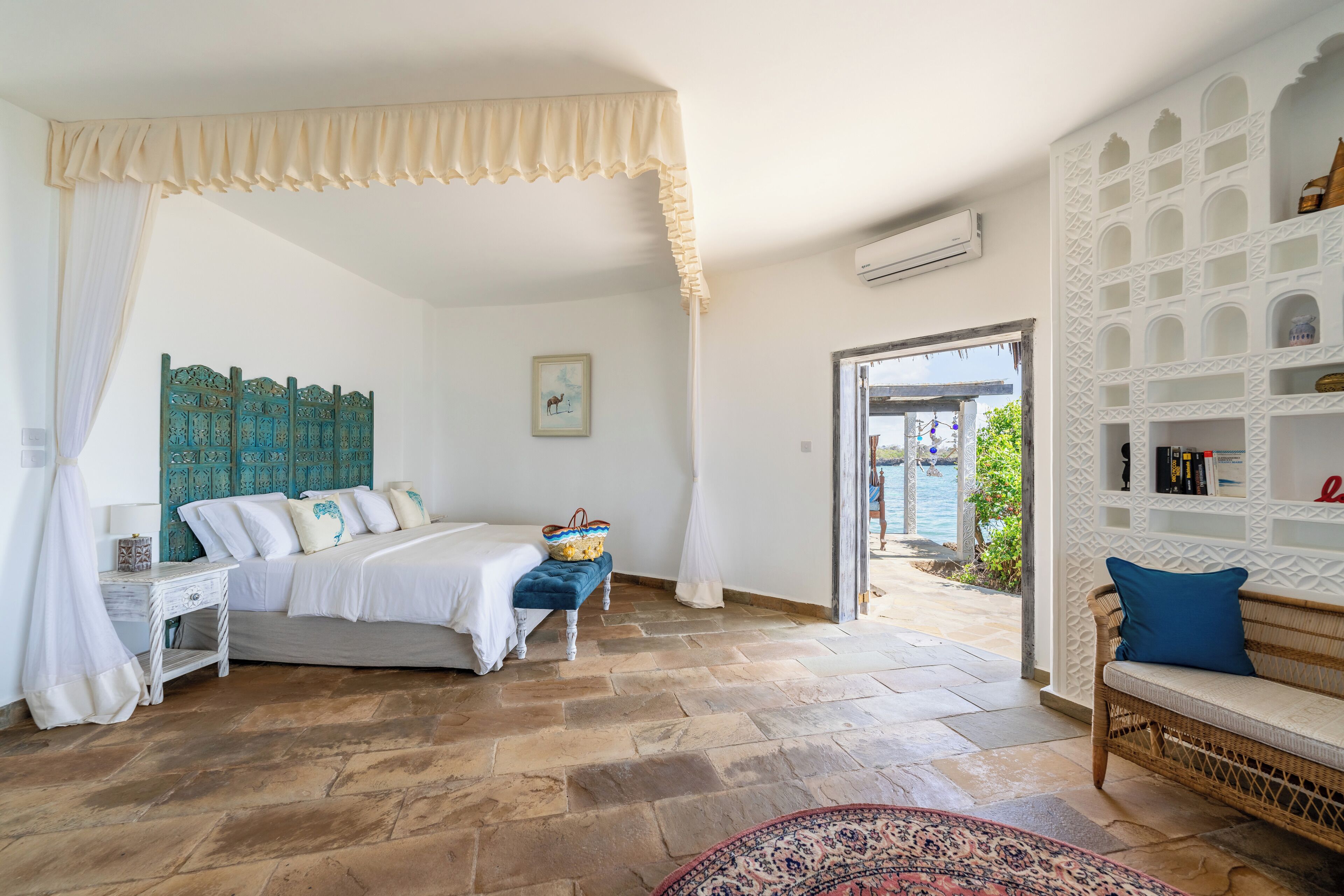 A bedroom with a bed, bedside table, and a view of the outside.