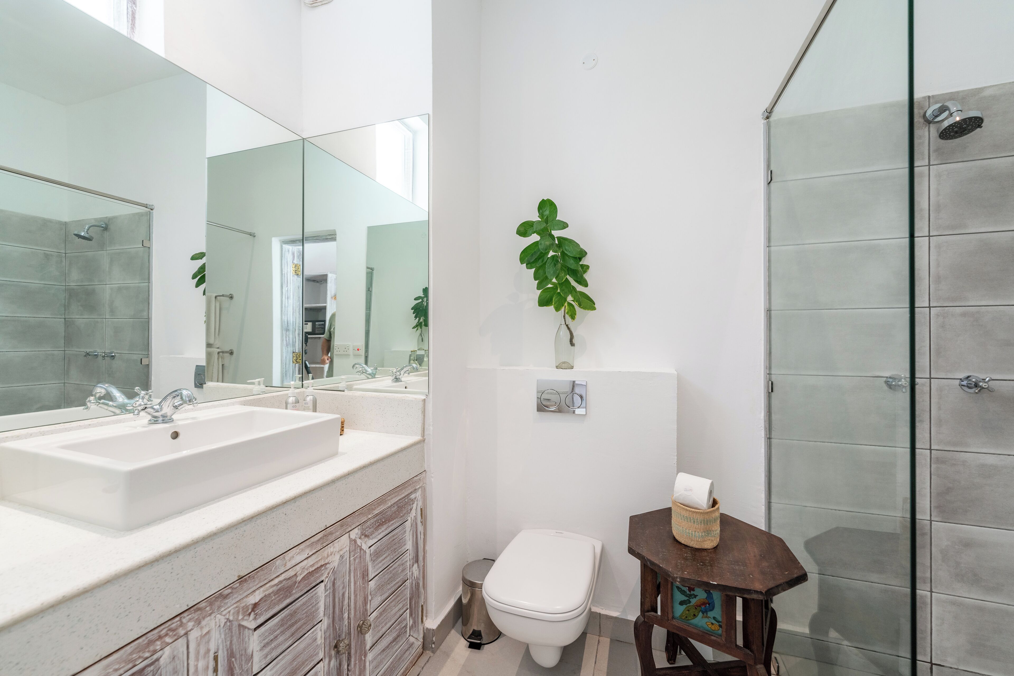 Un baño moderno con un espejo grande, un lavamanos, un inodoro y una ducha.