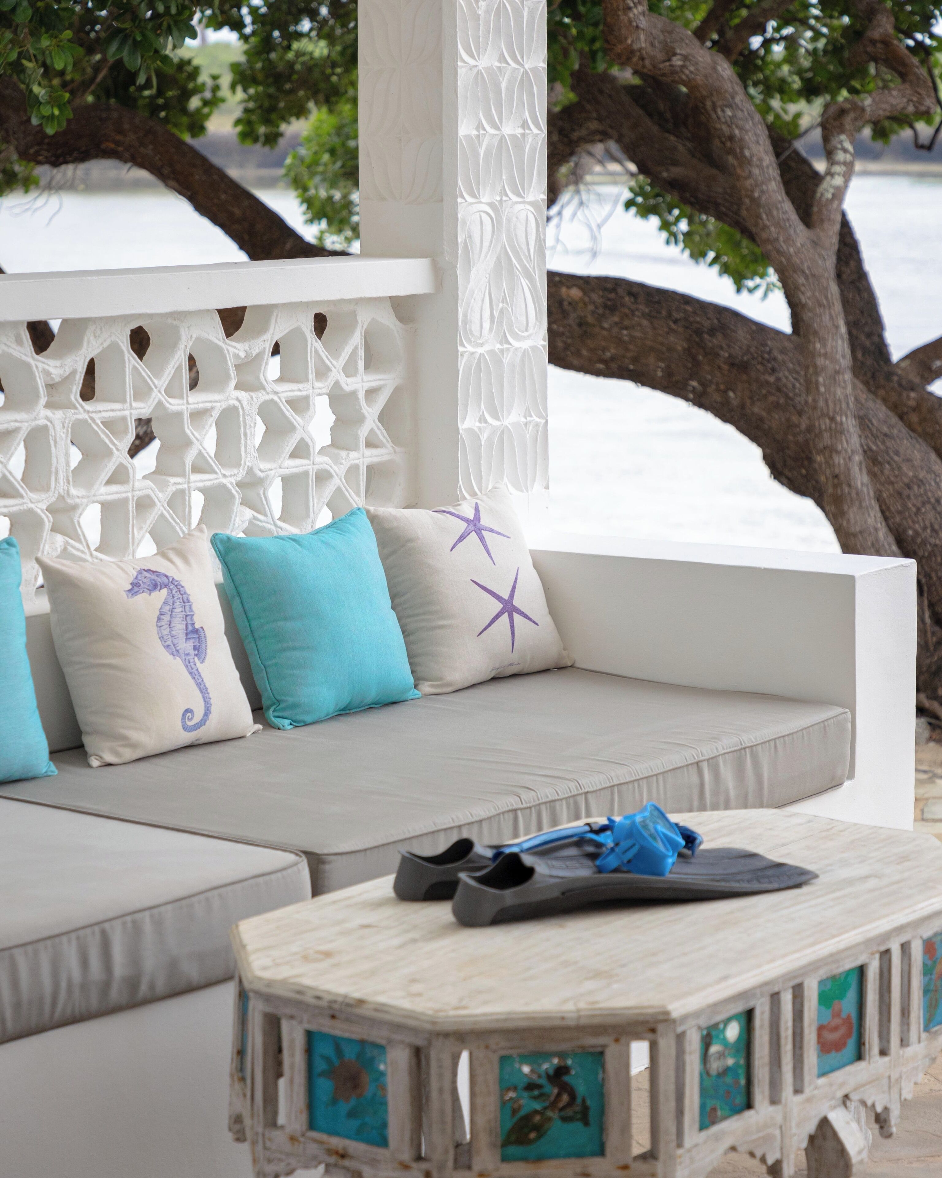 A white outdoor seating area with cushions and a small table with decorative tiles.
