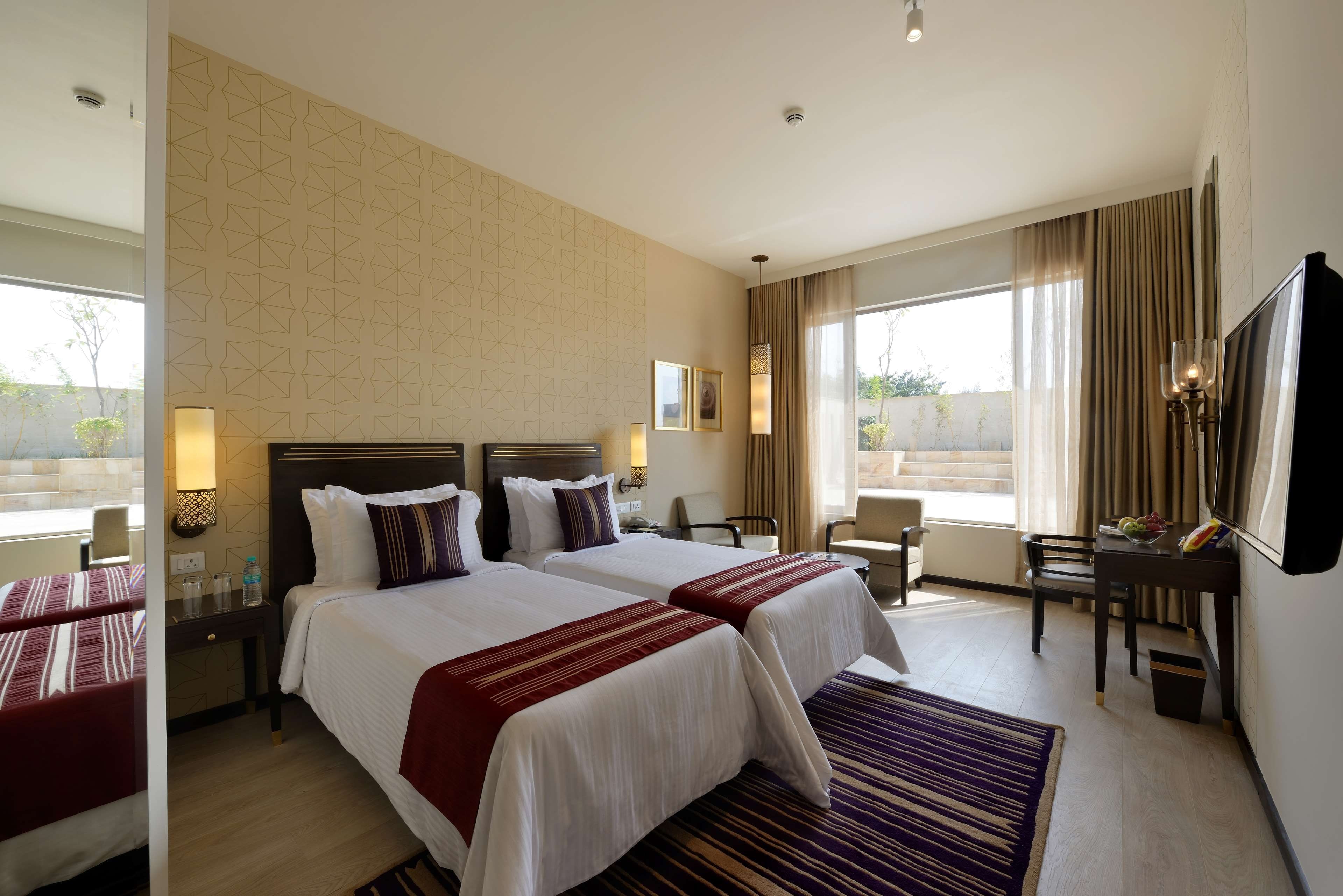 A hotel room with two beds, a desk, a chair, a TV, and a large window.