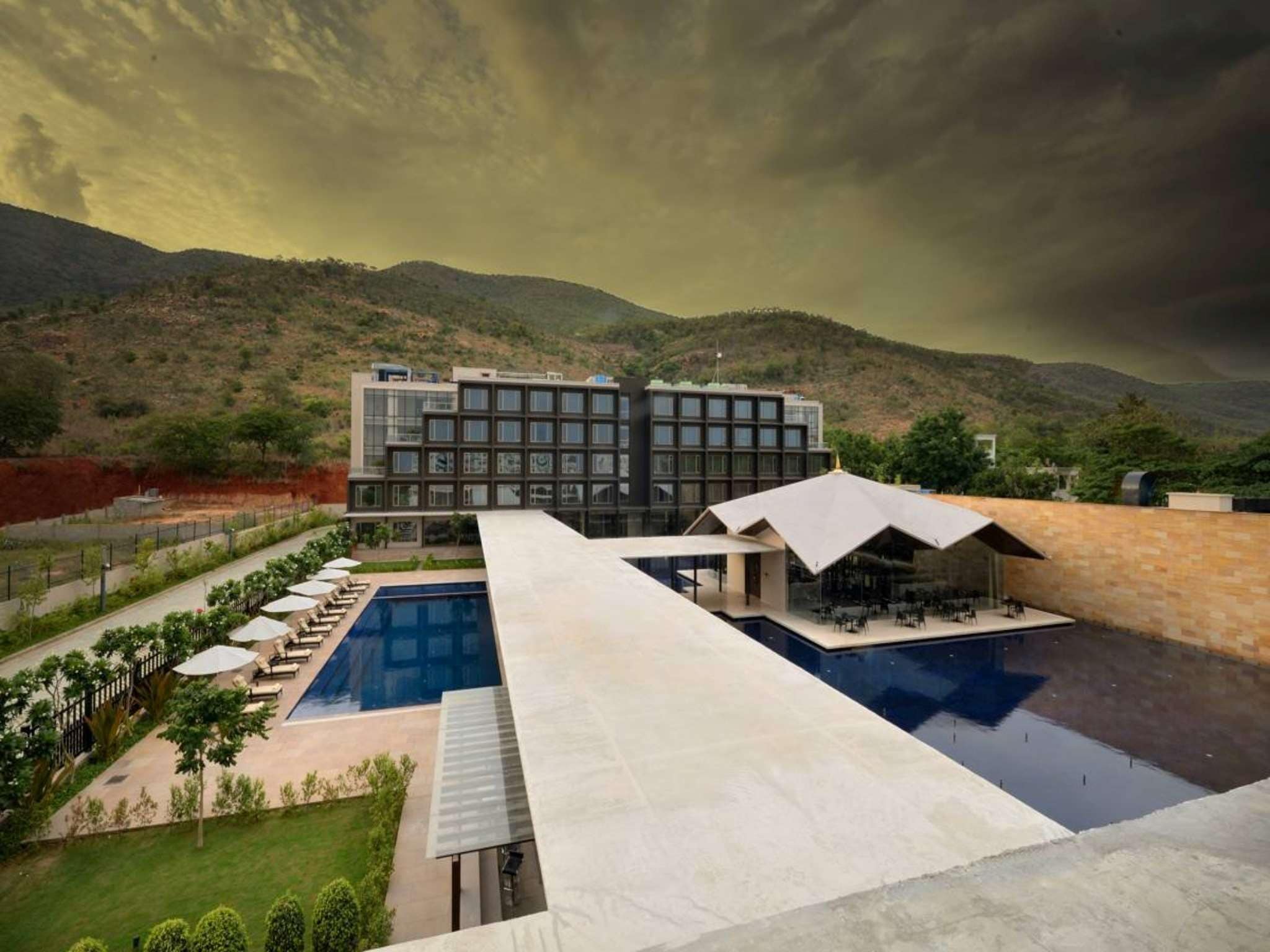 A modern hotel with a swimming pool, outdoor seating, and a view of the surrounding hills.