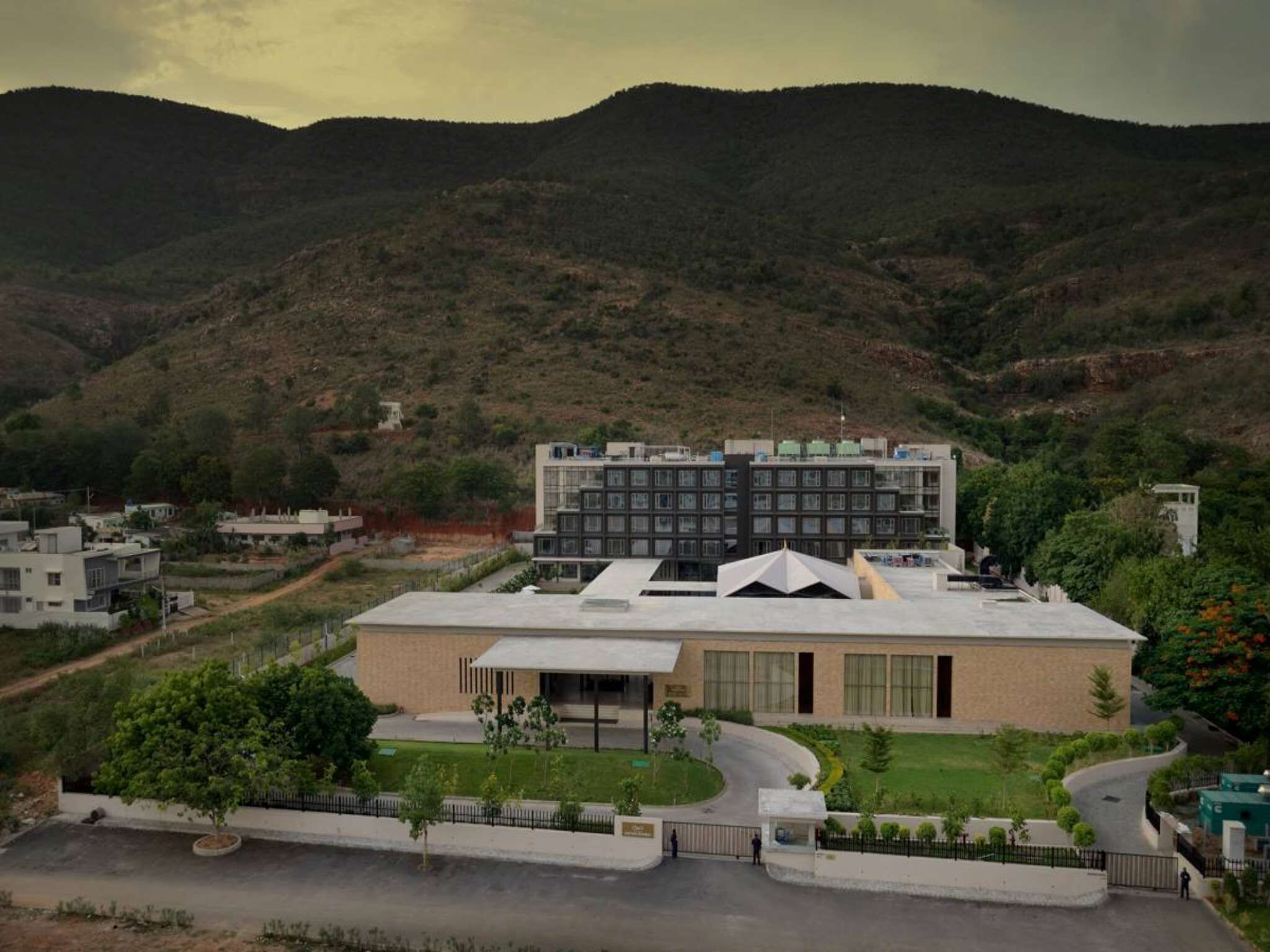 A modern building with a flat roof, surrounded by greenery and hills.