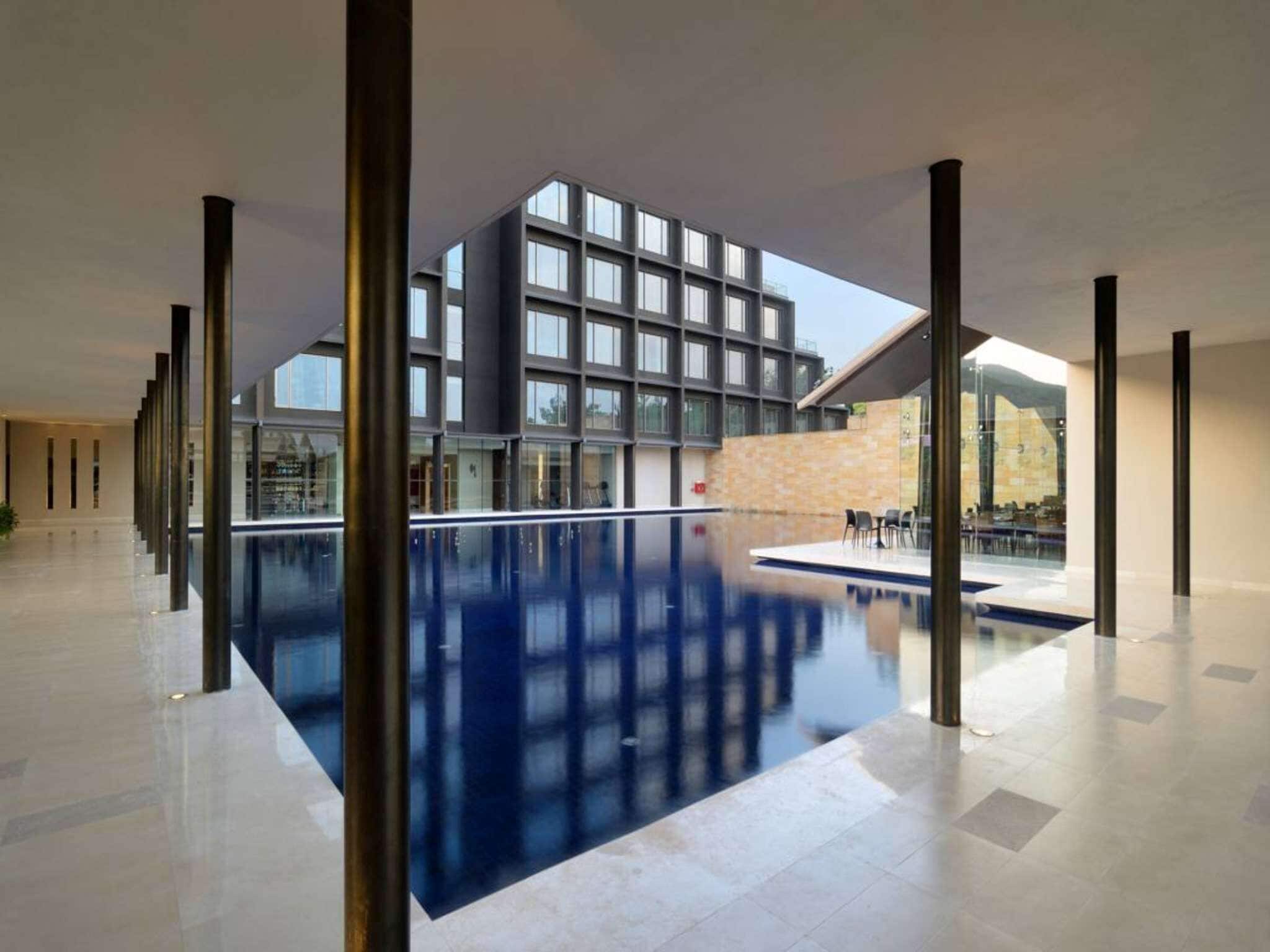 Una piscina interior moderna con vistas despejadas a un edificio con amplios ventanales y una pared de piedra.