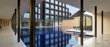 Una piscina interior moderna con vistas despejadas a un edificio con amplios ventanales y una pared de piedra.