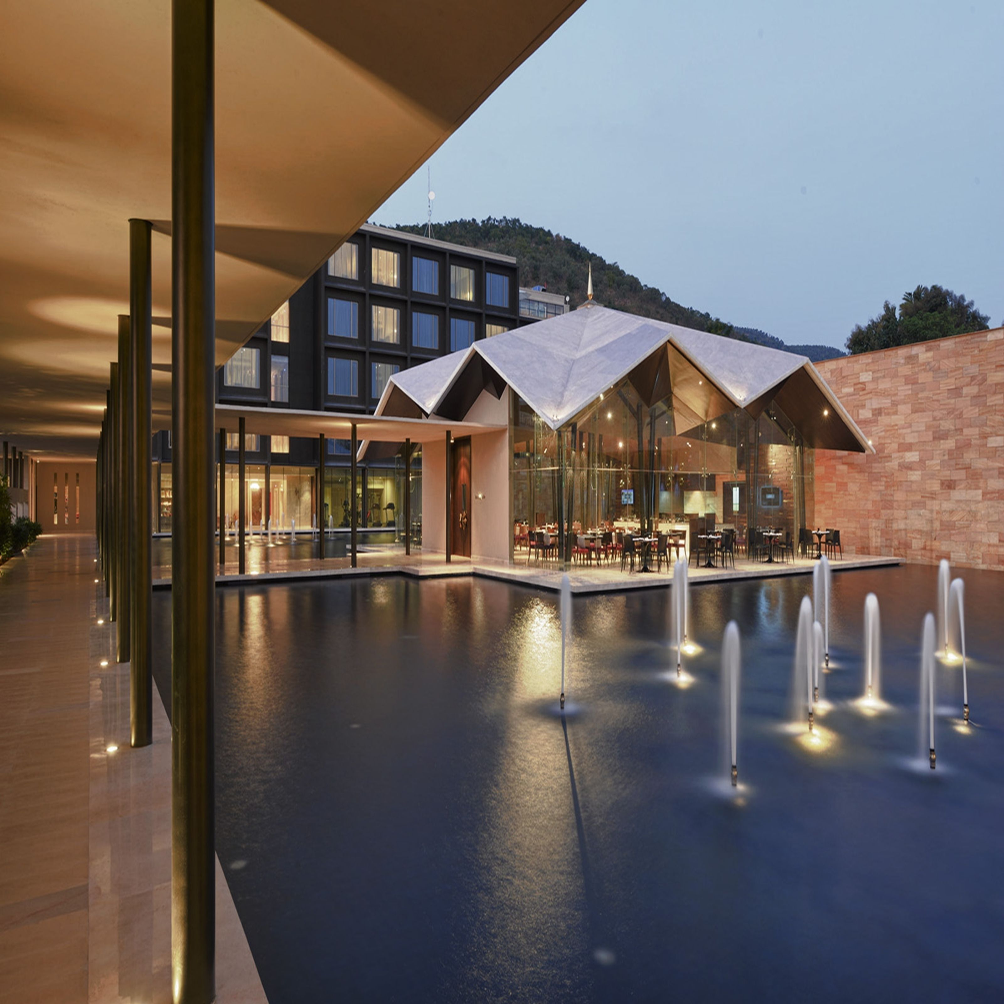A modern building with a pool area, outdoor seating, and a mountain backdrop.