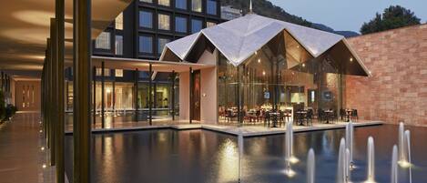 A modern building with a pool area, outdoor seating, and a mountain backdrop.