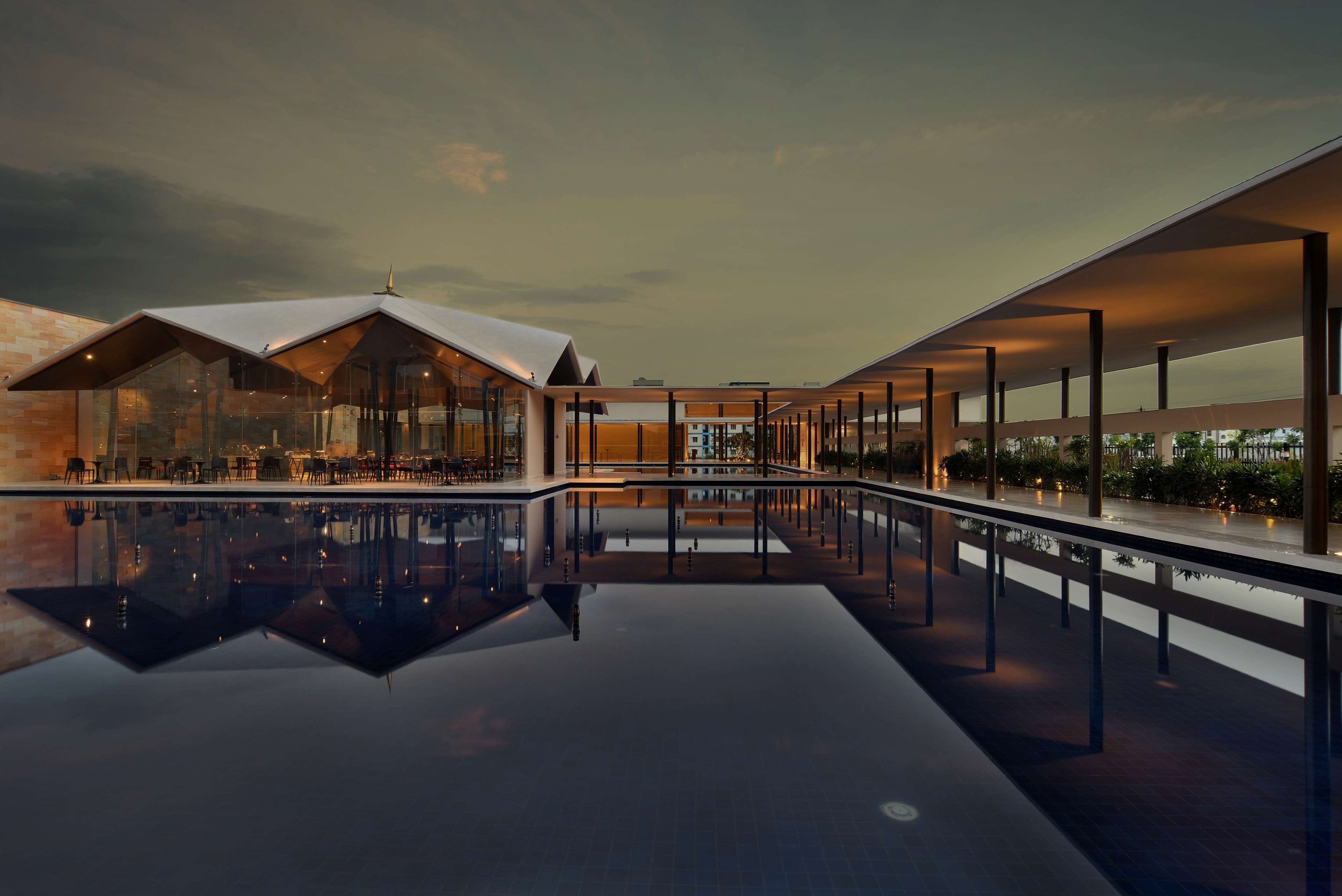 A modern building with a glass facade, a pool, and outdoor seating areas.