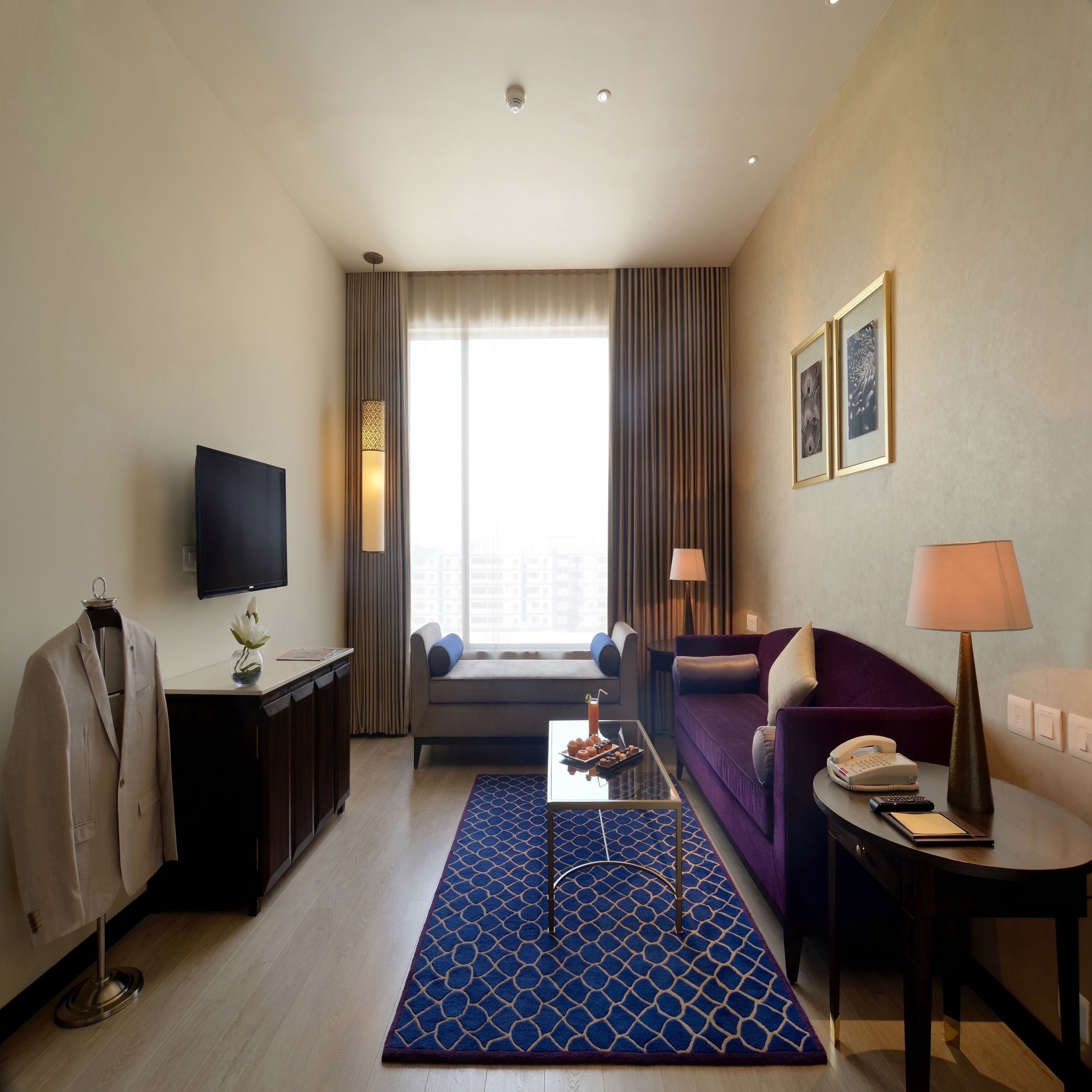 A hotel room with a flat-screen TV, a sofa, a coffee table, a desk with a lamp, and a bed.