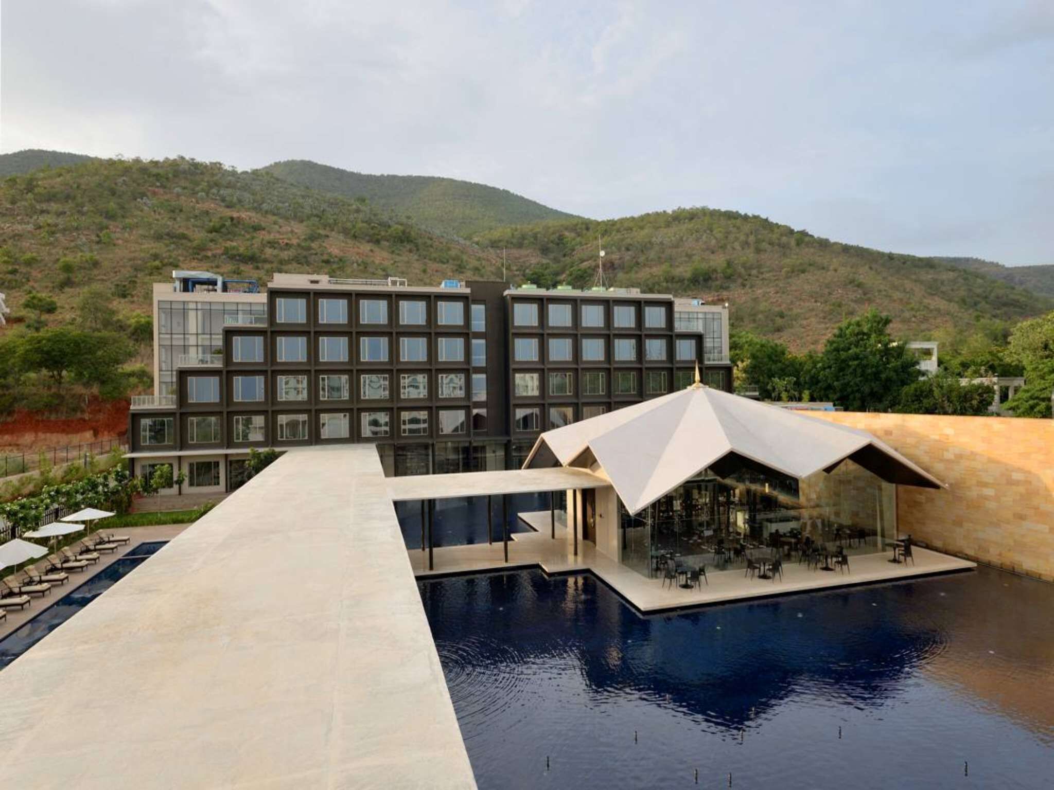 Un hotel moderno con piscina, mobiliario exterior y vistas a colinas.