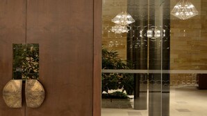 A modern lobby with a wooden door, a glass wall reflecting interior lights, and a potted plant. - Marasa Sarovar Premiere Tirupati (Tirupati)