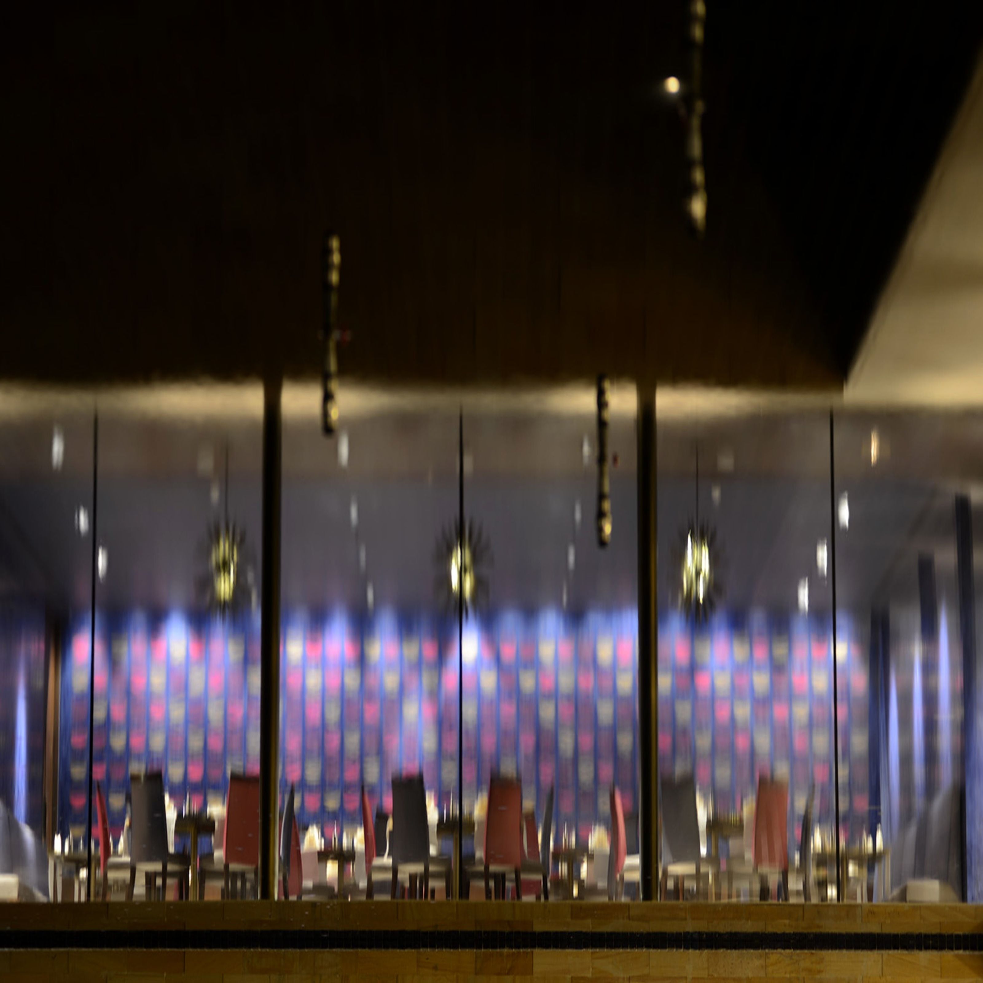 A modern interior with a row of tables and chairs, overhead lighting, and a patterned backdrop.