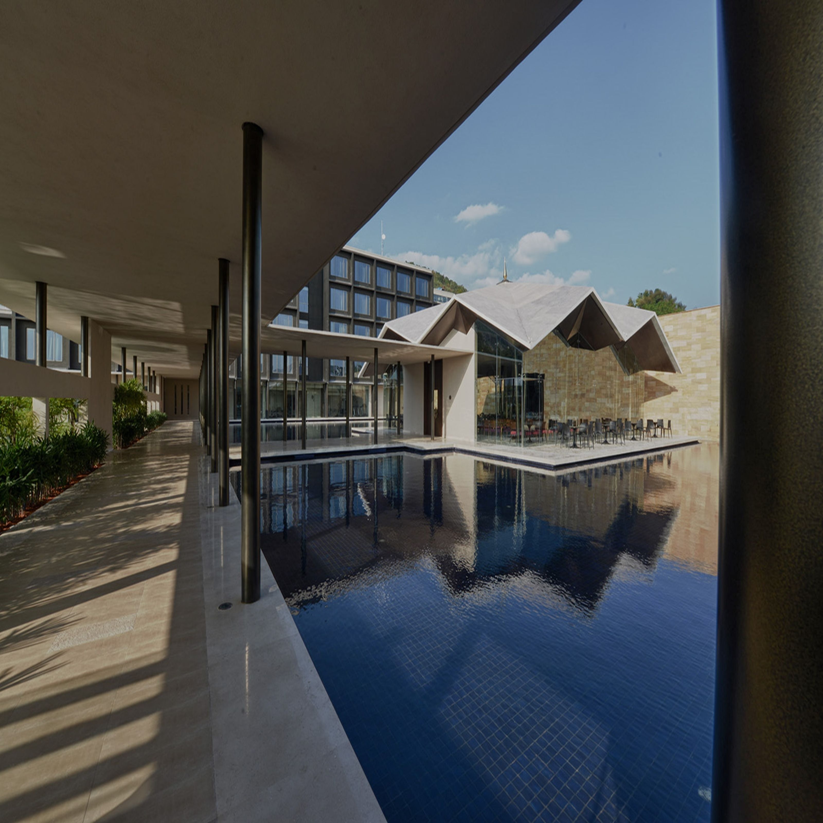 A modern building with a swimming pool, large windows, and a clear sky.
