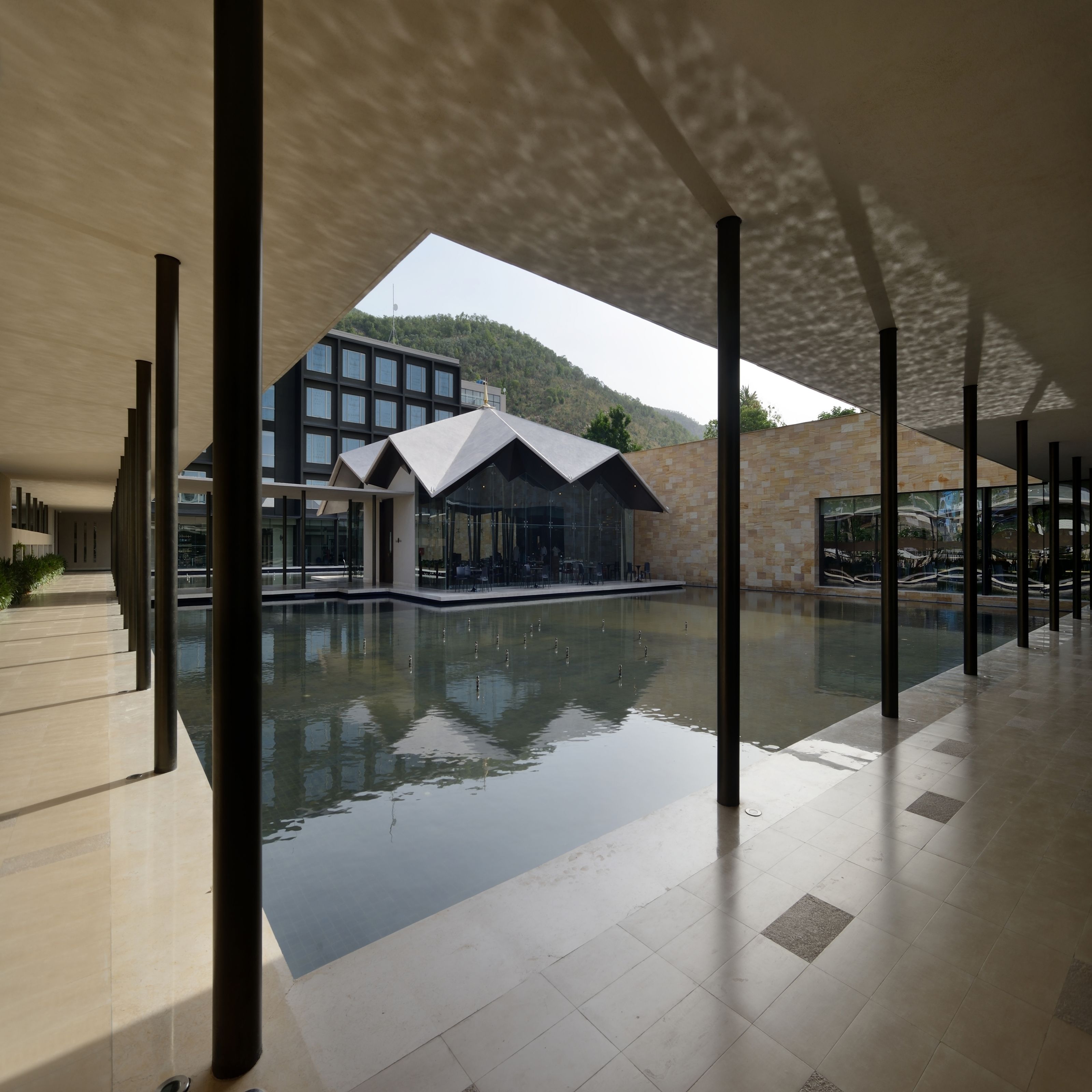 A modern building with a reflective pool, large windows, and a mountainous backdrop.