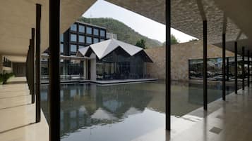 A modern building with a reflective pool, large windows, and a mountainous backdrop.