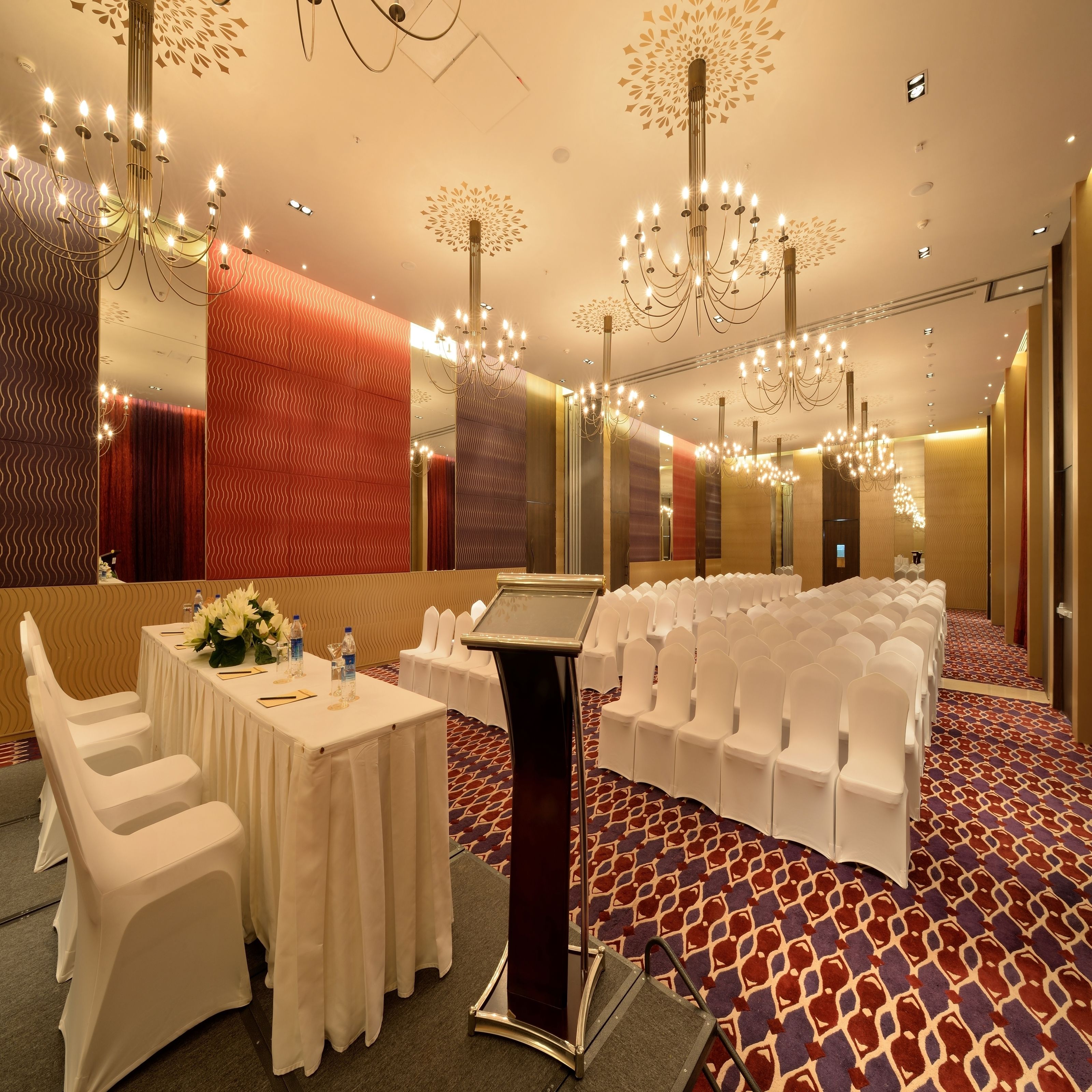 A conference room with white chairs, a table with water bottles, and a large mirror.