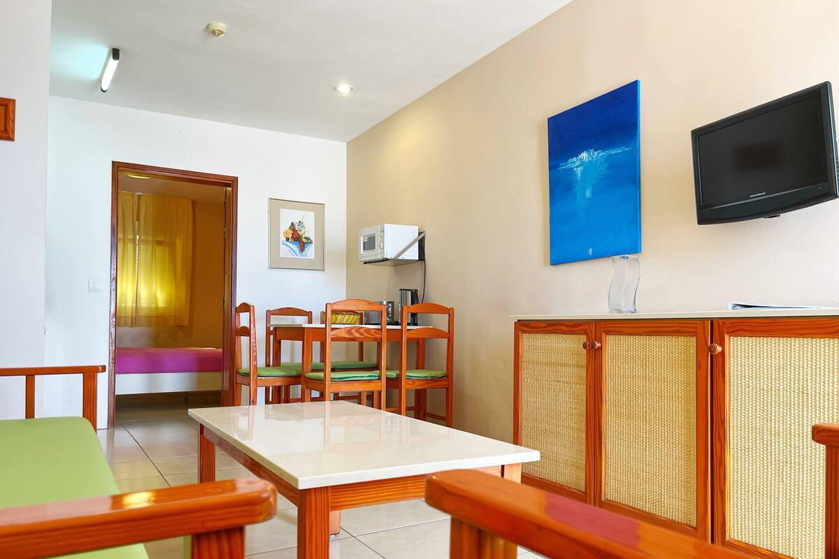 A hotel room with a dining area, a TV mounted on the wall, and a window with a view.