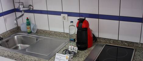Et køkken med en stålvask, en rød elkedel, en kaffemaskine og et indbygget elektrisk komfur.