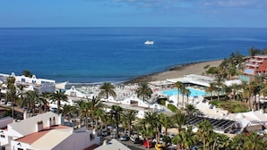 A coastal resort with a pool, palm trees, and a view of the sea. - Apartamentos Curasol (Mogan)