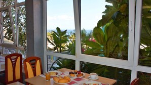 A breakfast table with plates of food, a cup of coffee, and a view of the ocean through large windows. - Apartamentos Curasol (Mogan)