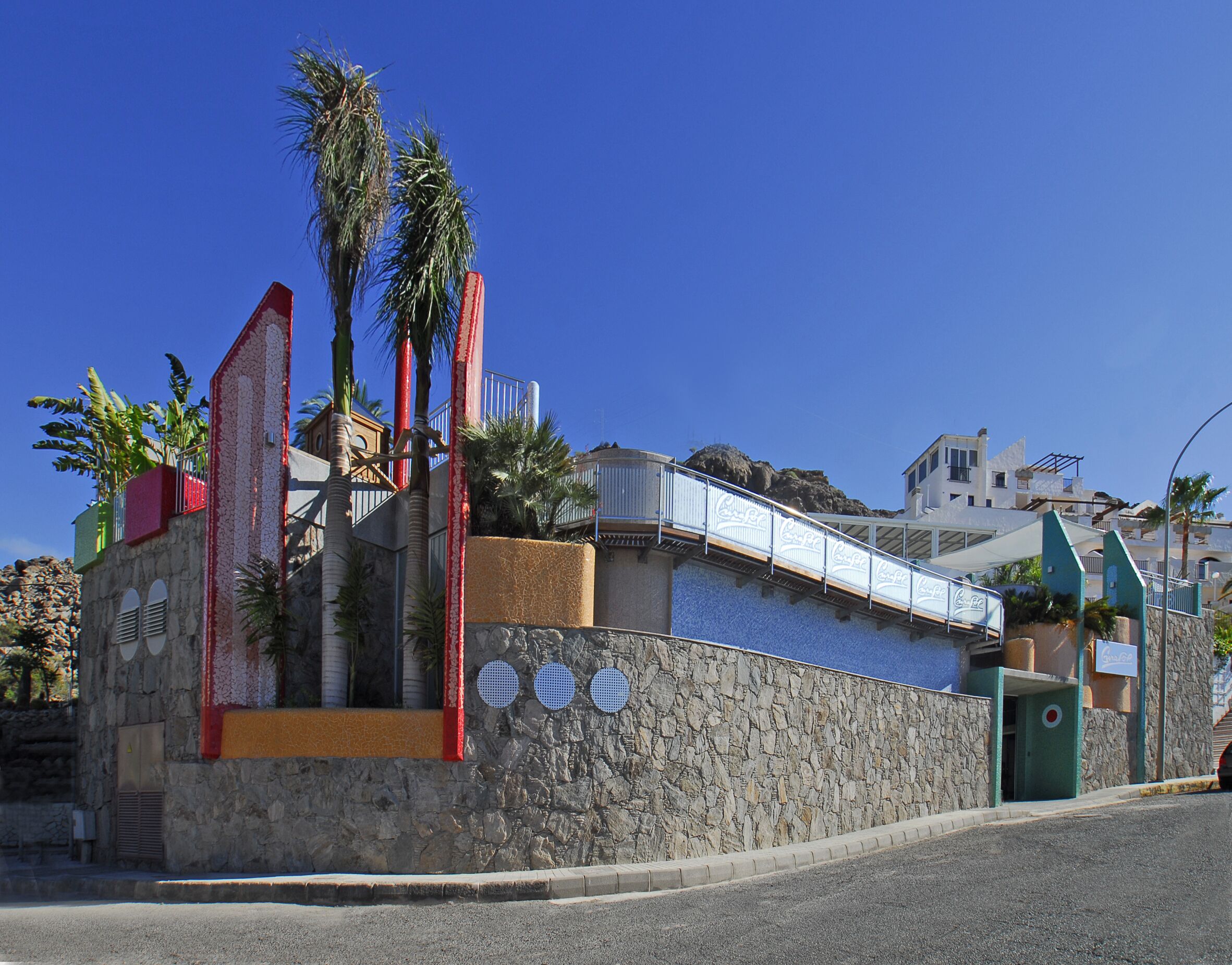A coastal building with a stone facade, palm trees, and a Coca-Cola sign.
