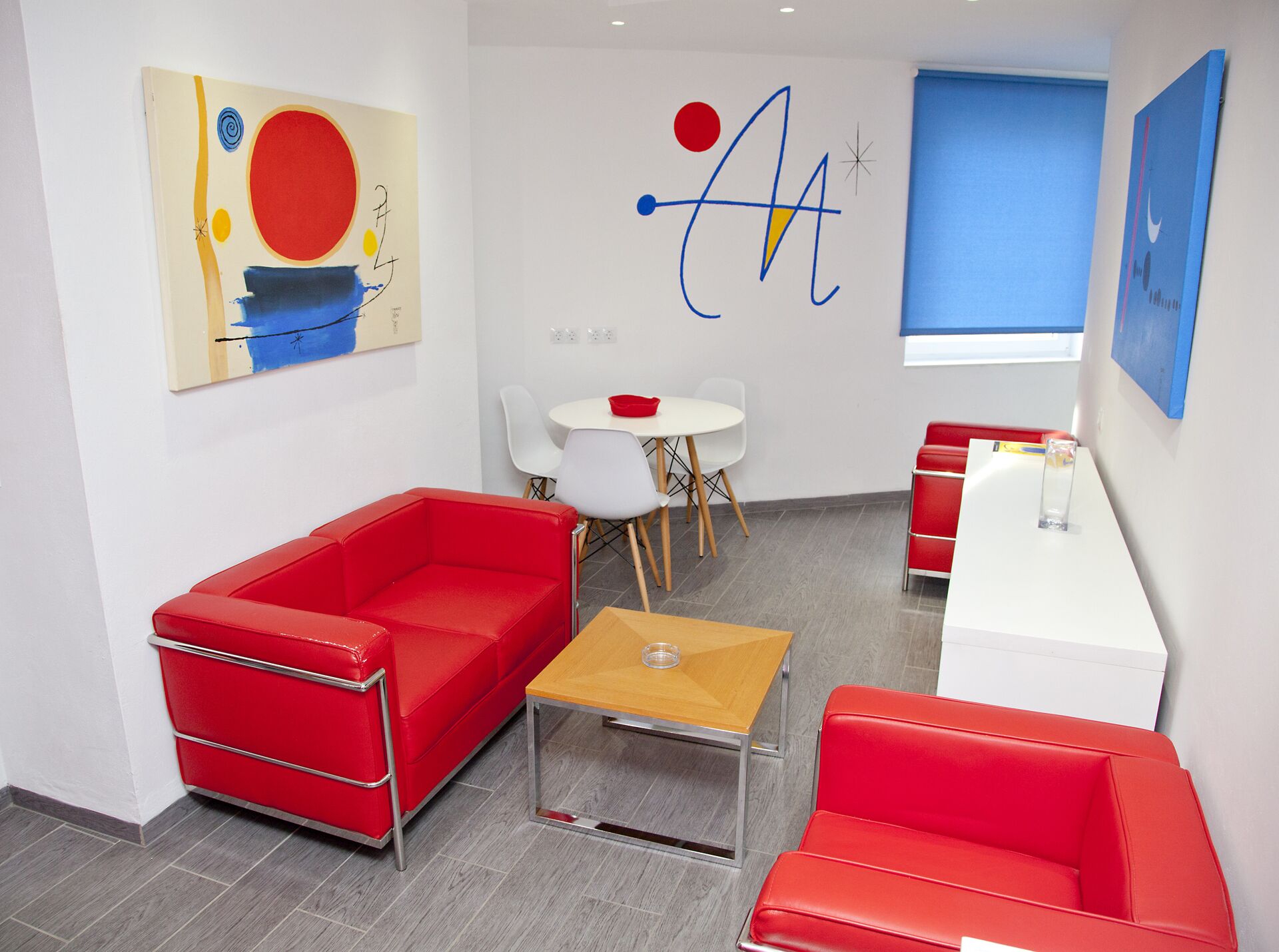 Ein modernes Zimmer mit roter Einrichtung, einem weißen Tisch und abstrakten Kunstwerken an den Wänden.
