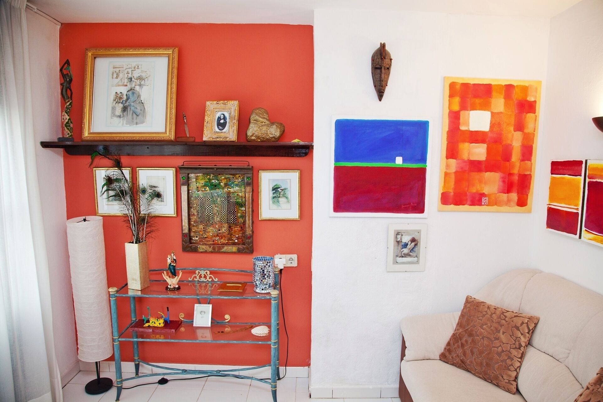 A living room with a red wall, a glass display unit, and a beige sofa.