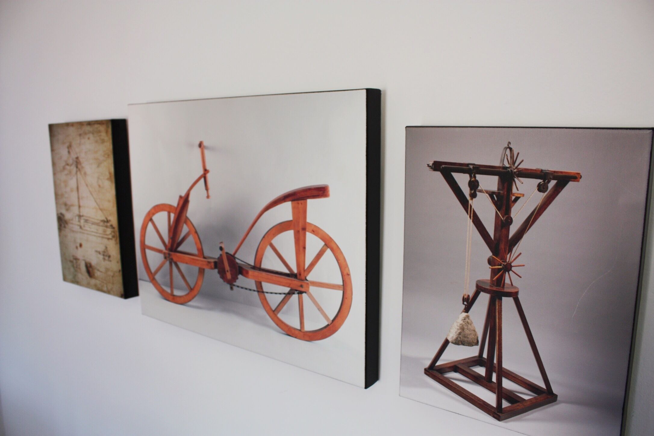 Drei gerahmte Kunstwerke: ein altes Fahrrad, eine rustikale Holzkonstruktion und ein abstraktes Werk mit Struktur.