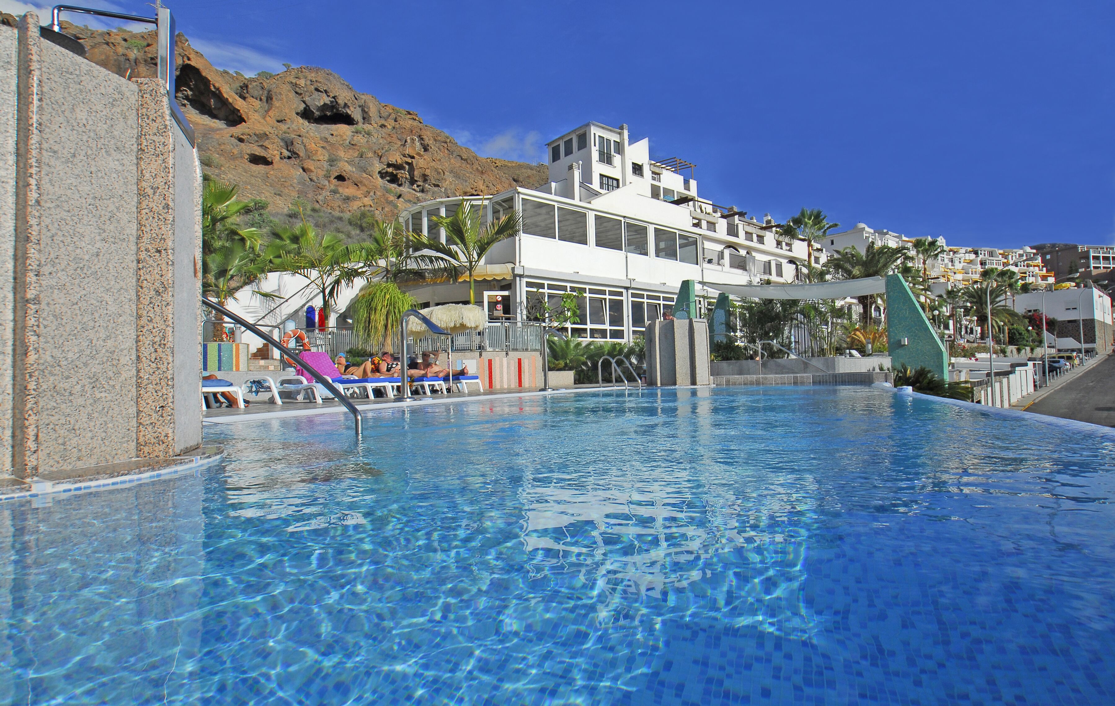 A swimming pool with clear blue water, surrounded by a modern building with multiple floors and balconies.