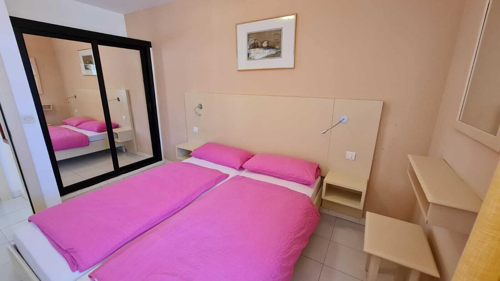 Une chambre à coucher avec un grand lit, un miroir, une table de chevet et un tableau encadré au mur.