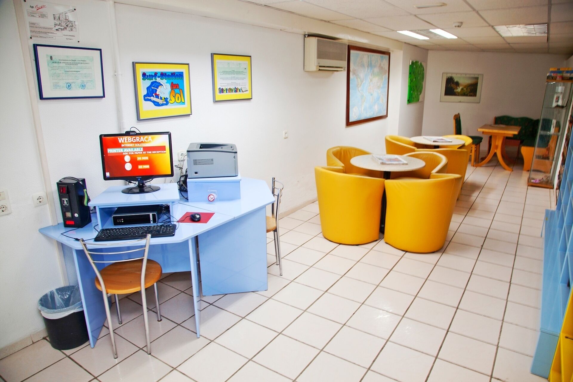 A reception area with a computer desk, printer, and yellow chairs.