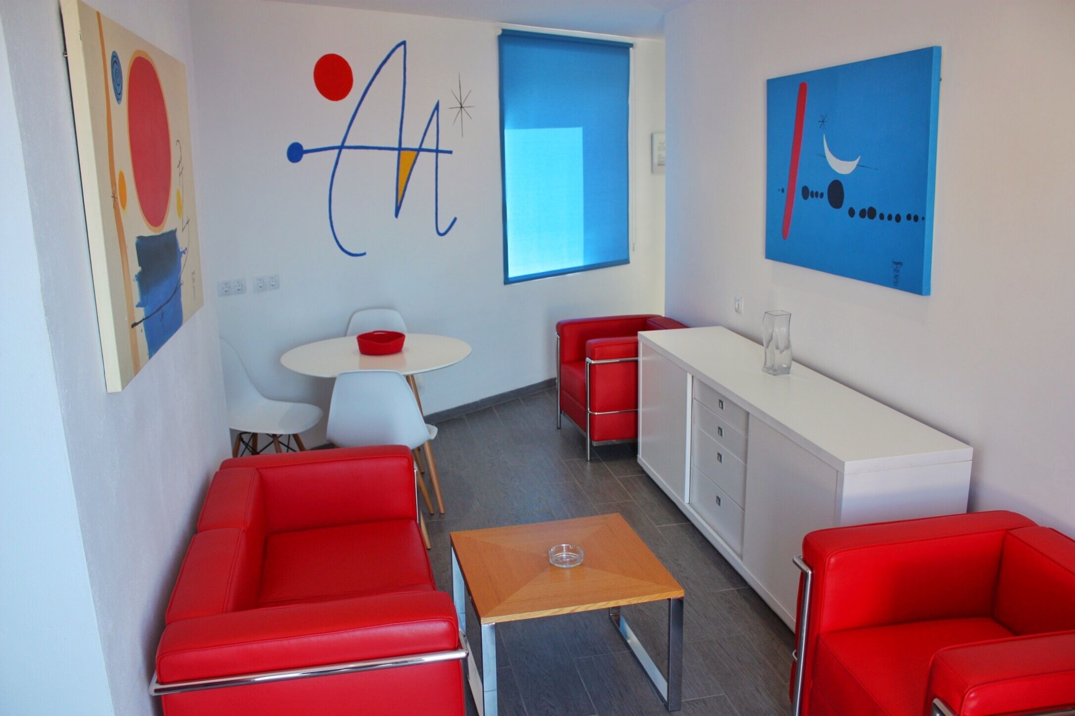 A modern kitchen with red and white furniture, a small dining table, and a window with a blue view.