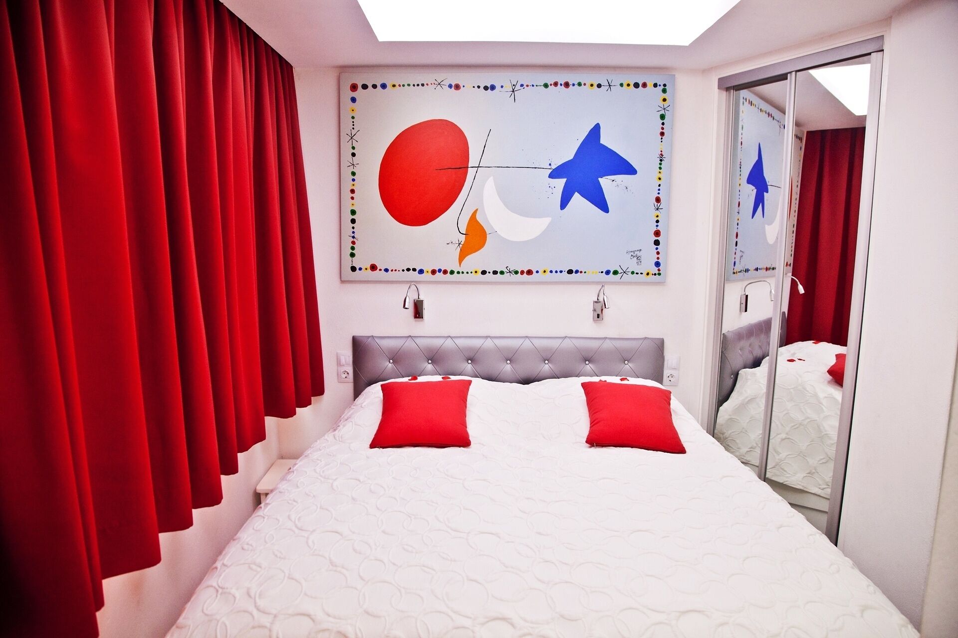 Une chambre moderne avec un grand lit, des rideaux rouges et une œuvre d’art murale originale.