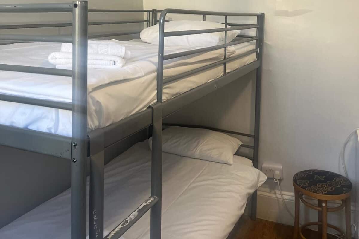 A bunk bed room with white bedding and a wooden stool.