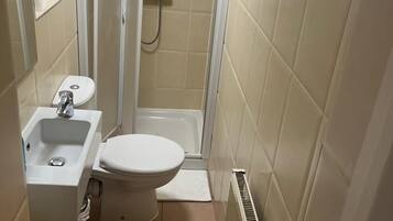 A small, compact bathroom with a toilet, sink, and shower stall.